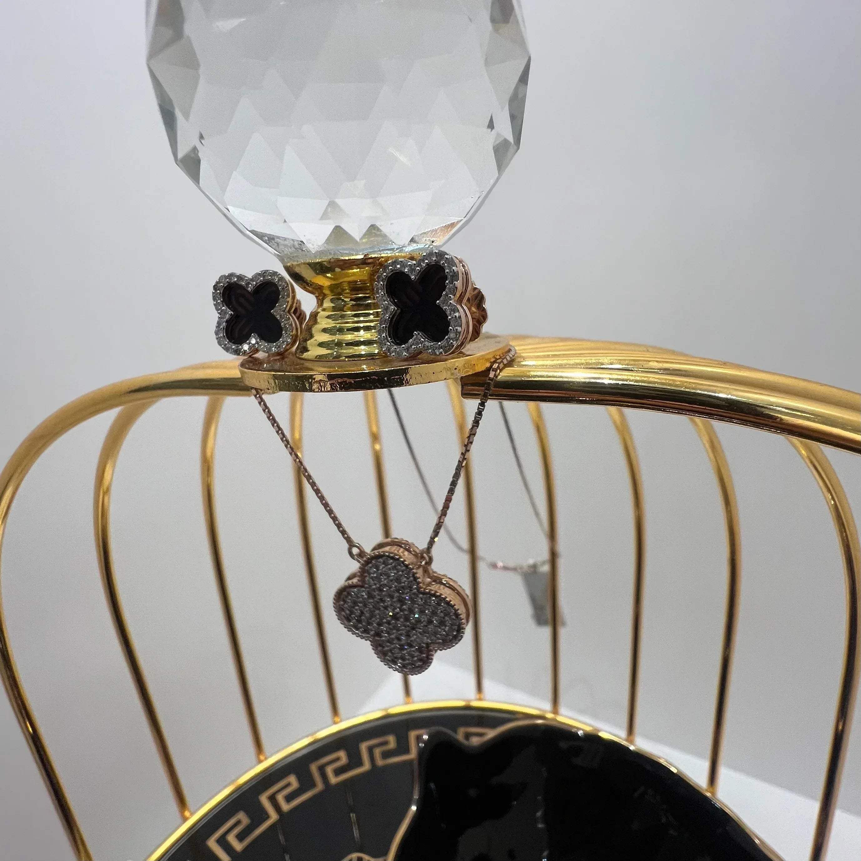 A gold diamond pendant with earrings set, featuring a chain of inset diamonds on a gold-colored metal structure, displayed on a glass stand.
