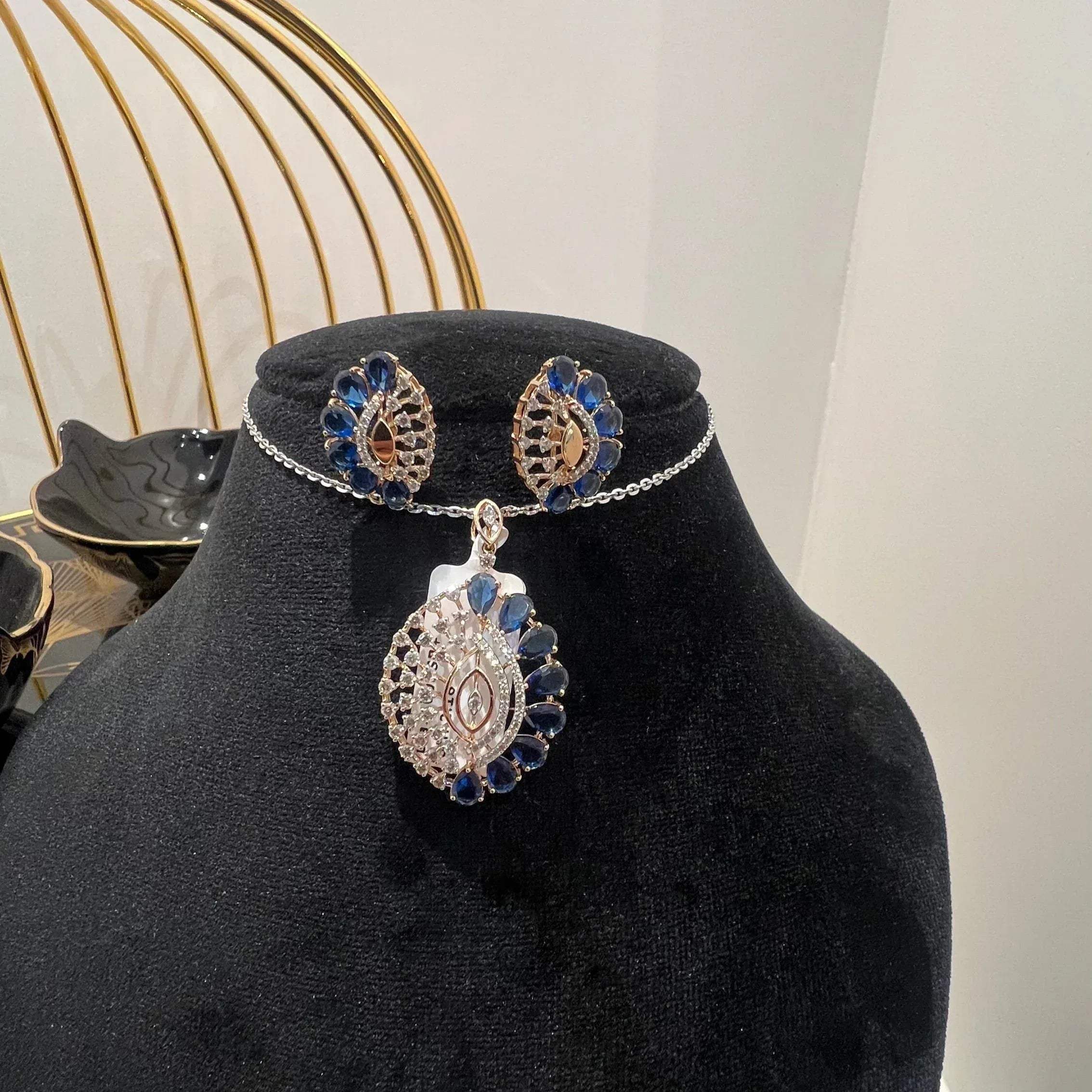 A gold diamond pendant with blue stone accompanied by matching earrings, displayed on a black mannequin bust.