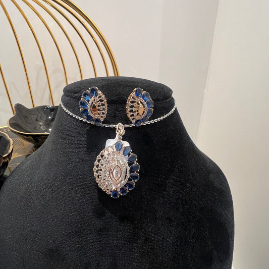 A gold diamond pendant with blue stone accompanied by matching earrings, displayed on a black mannequin bust.