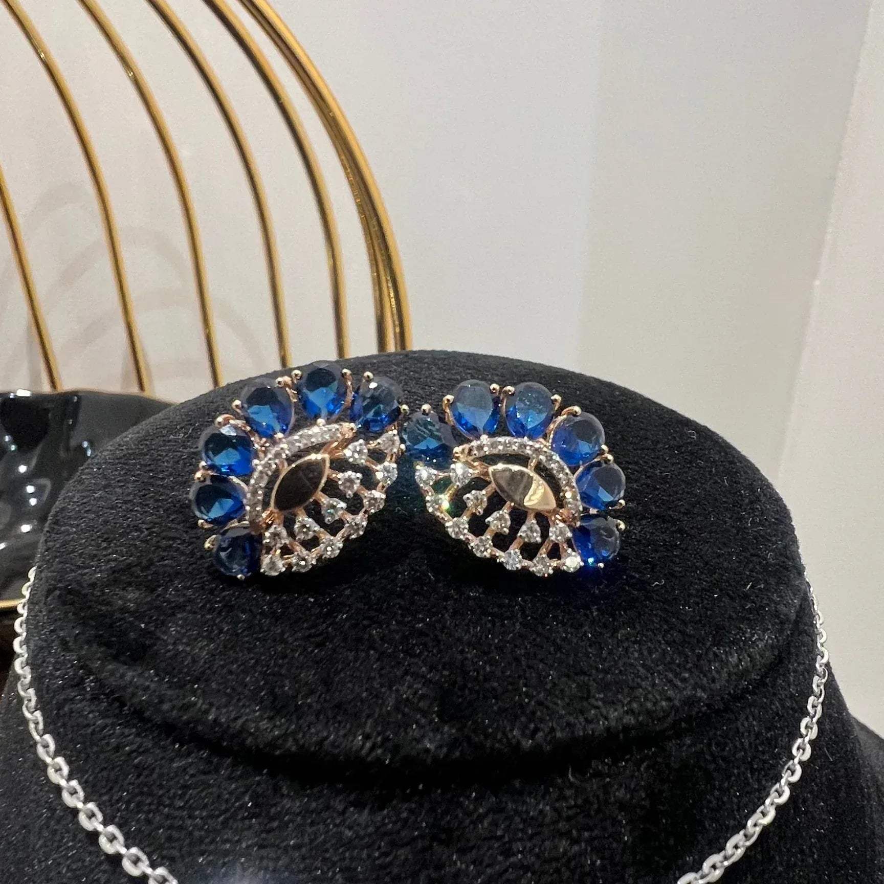 A gold diamond pendant with blue stone accompanied by matching earrings, displayed on a black mannequin bust.
