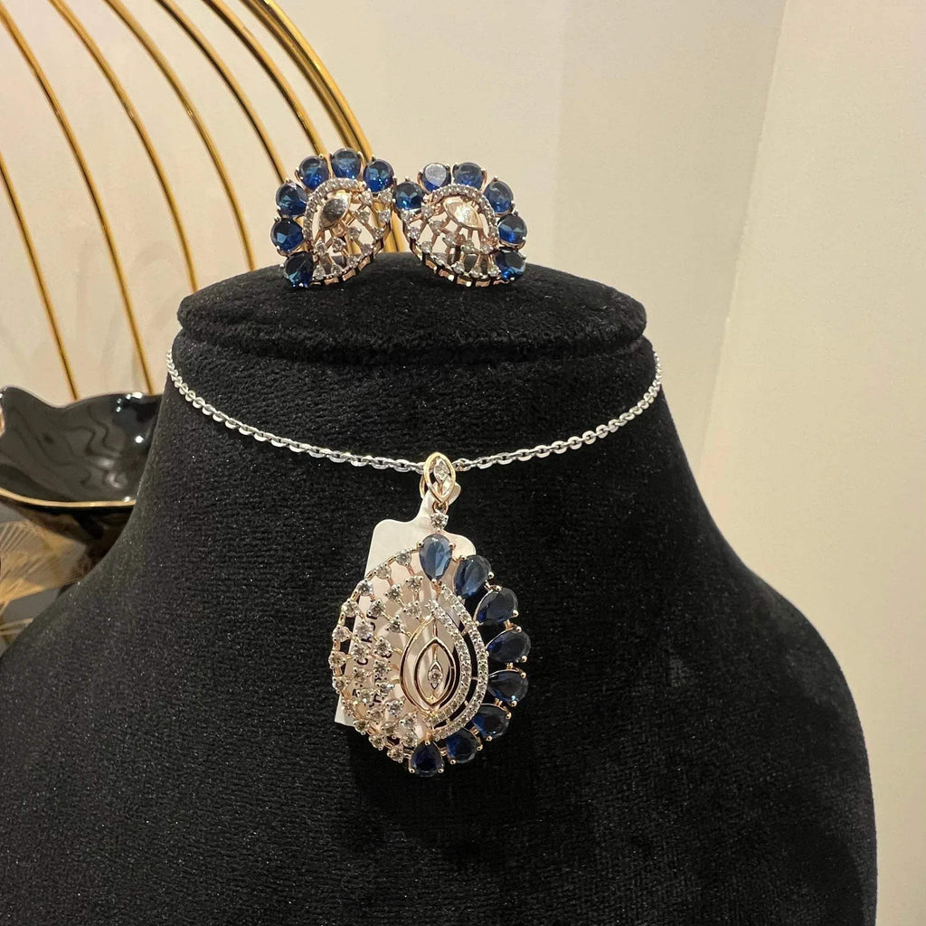 A gold diamond pendant with blue stone accompanied by matching earrings, displayed on a black mannequin bust.
