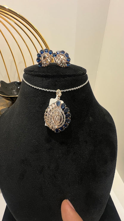 A gold diamond pendant with blue stone accompanied by matching earrings, displayed on a black mannequin bust.