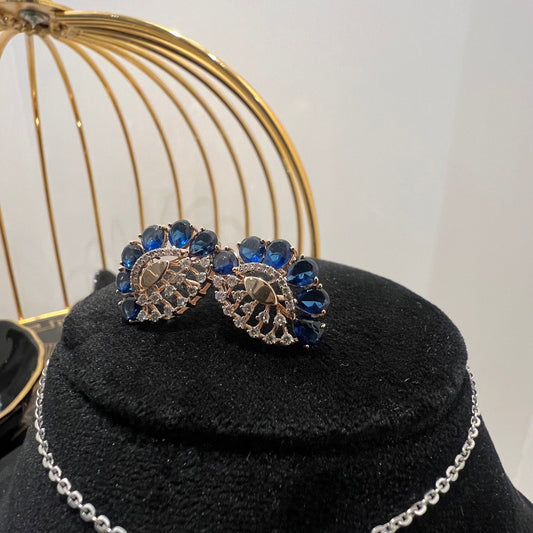 A gold diamond pendant with blue stone accompanied by matching earrings, displayed on a black mannequin bust.