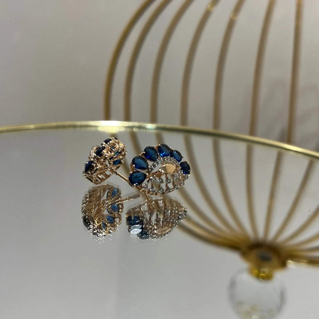 gold diamond earrings with blue stones, displayed on a table.