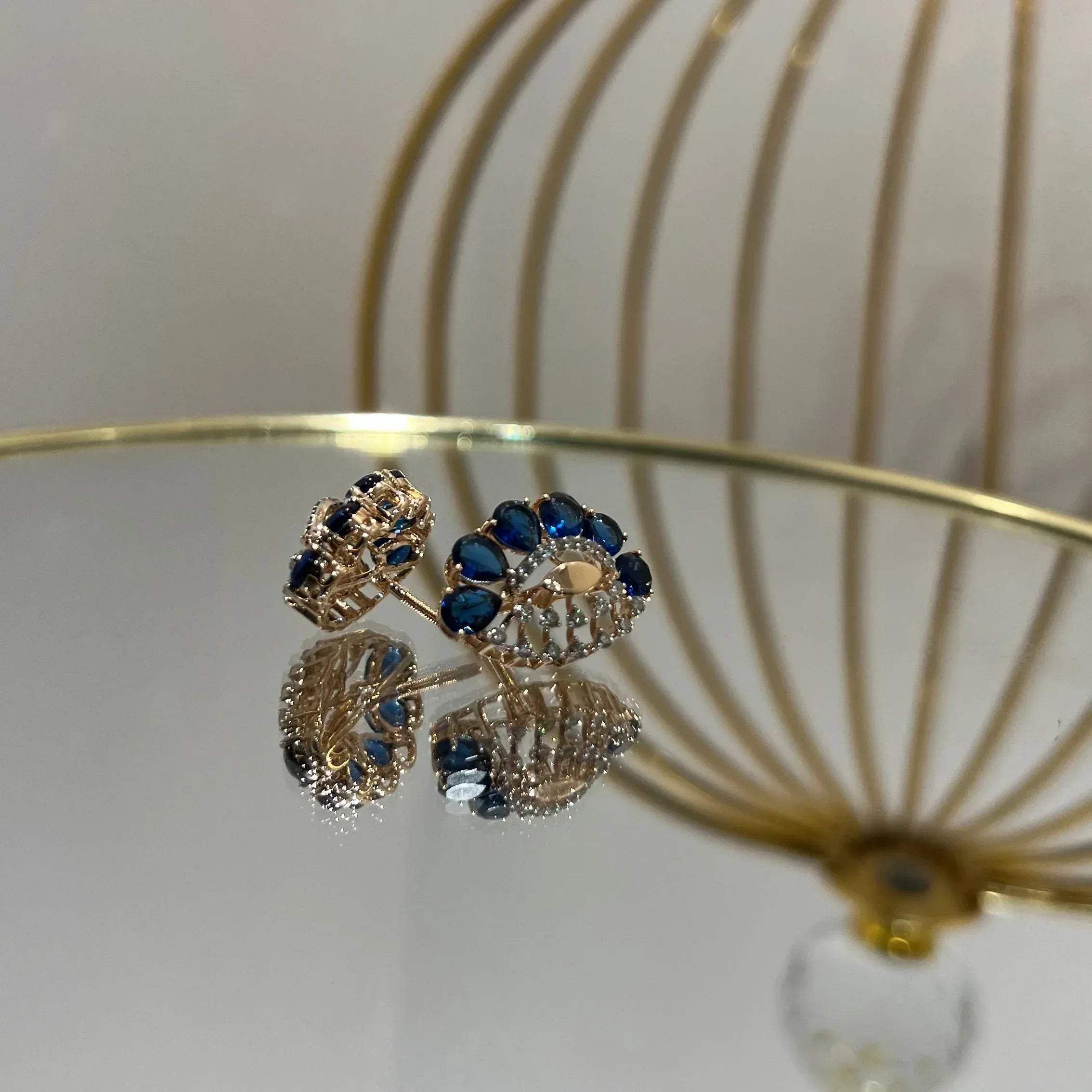 gold diamond earrings with blue stones, displayed on a table.