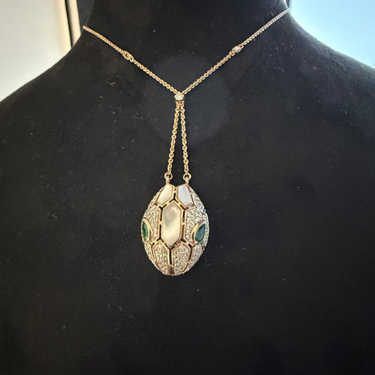 A gold diamond pendant with a chain, featuring a white and green stone in a gold setting.