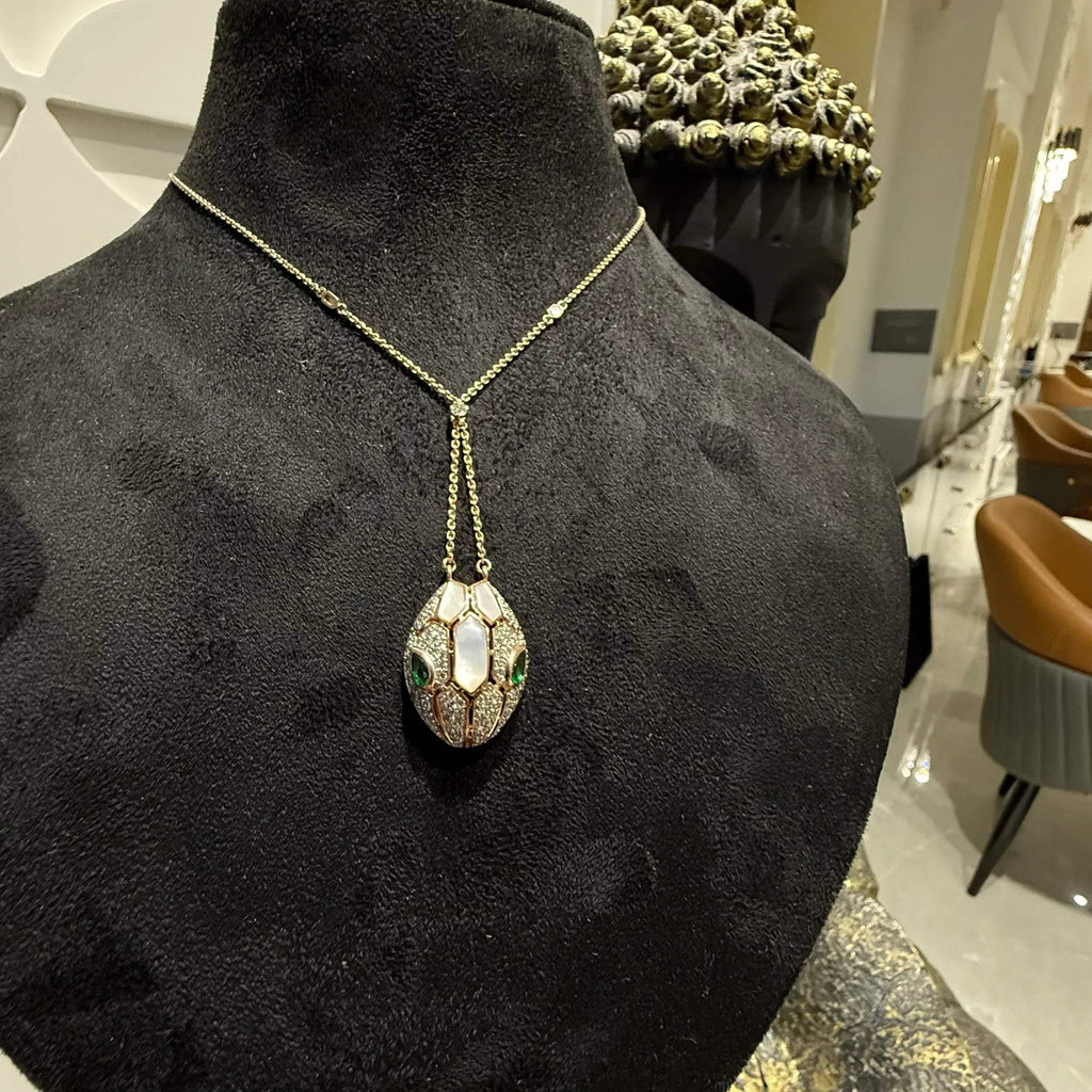 Oval-shaped gold diamond pendant with emerald green accents and mosaic design on a fine gold chain.