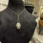 Oval-shaped gold diamond pendant with emerald green accents and mosaic design on a fine gold chain.