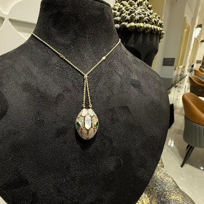 Oval-shaped gold diamond pendant with emerald green accents and mosaic design on a fine gold chain.
