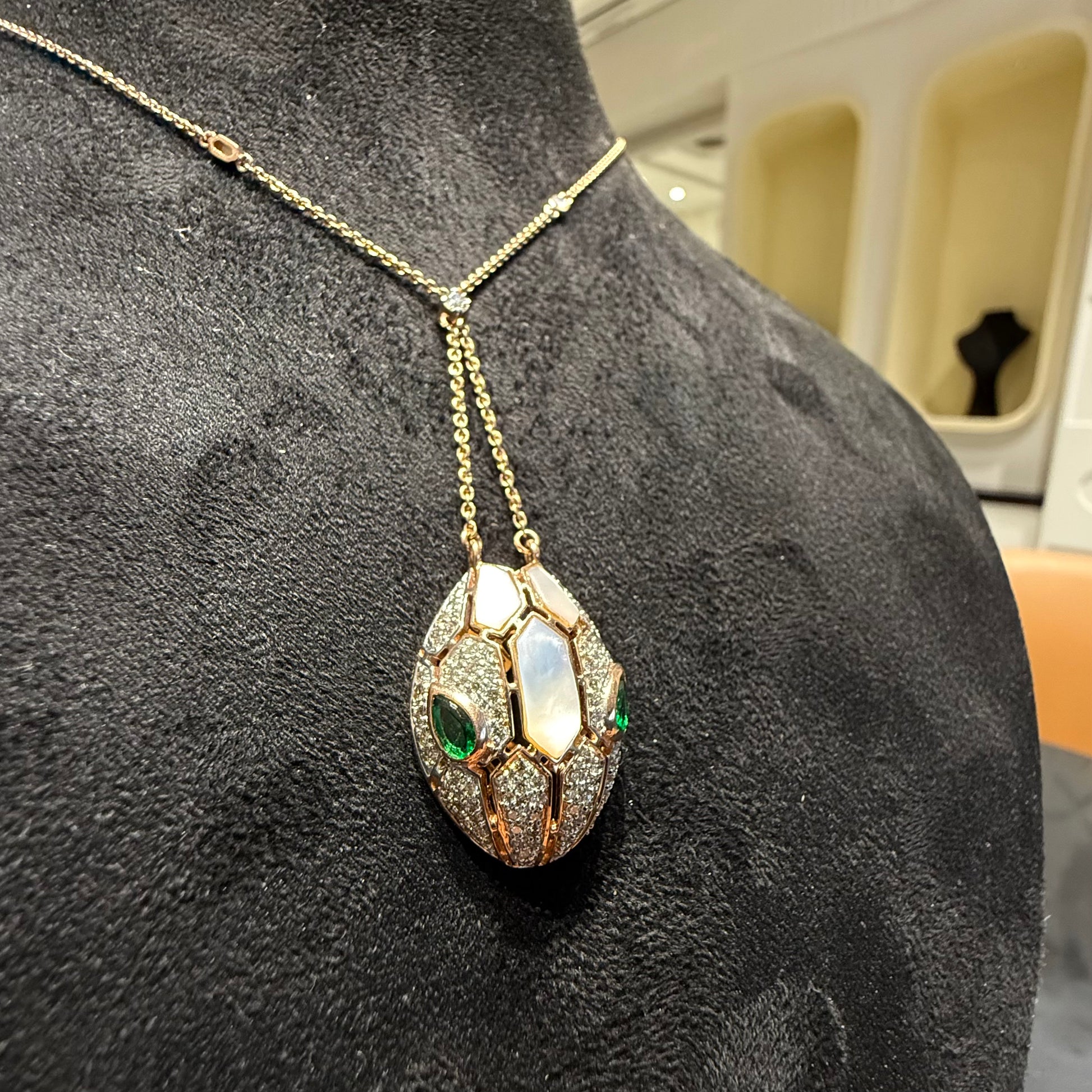 Oval-shaped gold diamond pendant with emerald green accents and mosaic design on a fine gold chain.