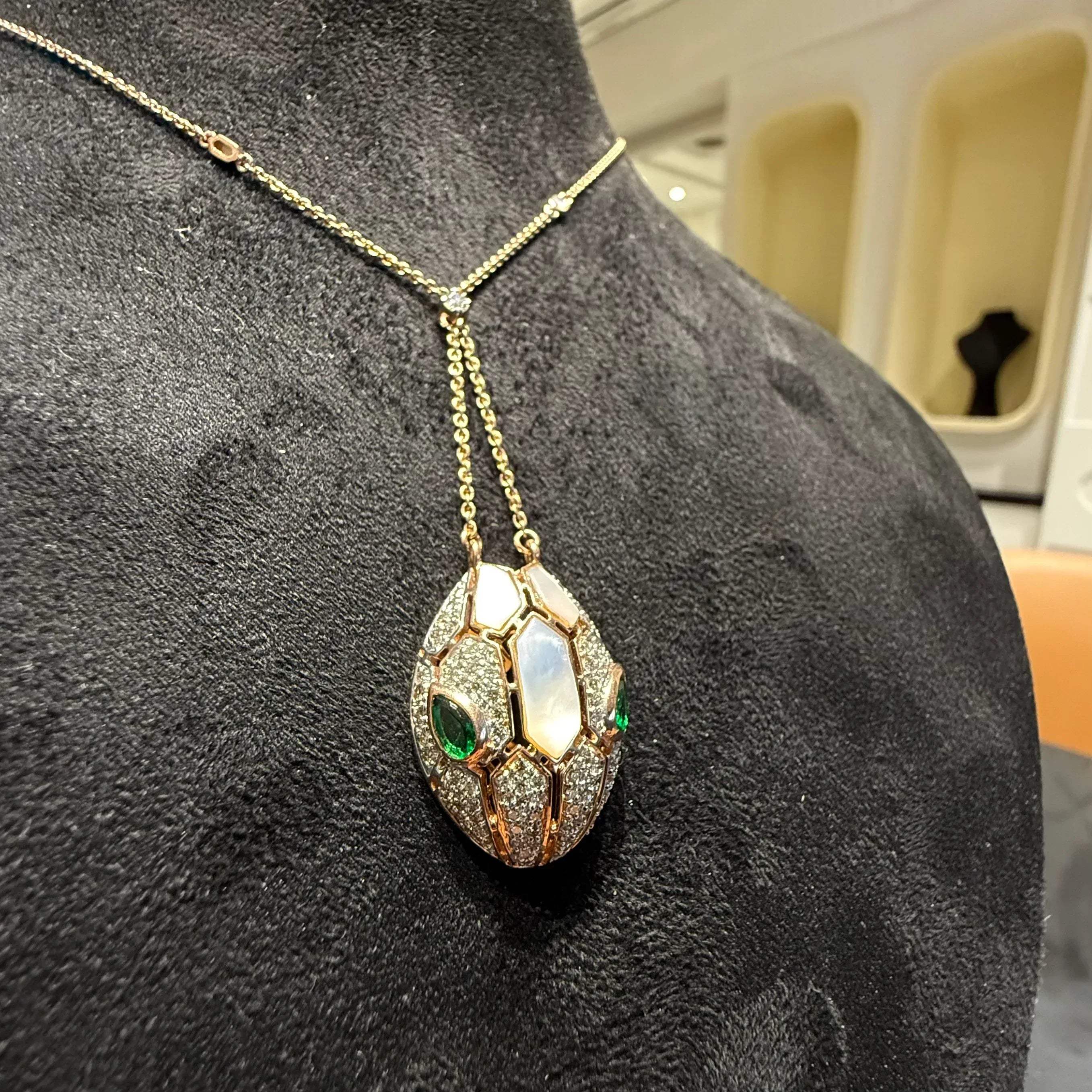 Oval-shaped gold diamond pendant with emerald green accents and mosaic design on a fine gold chain.