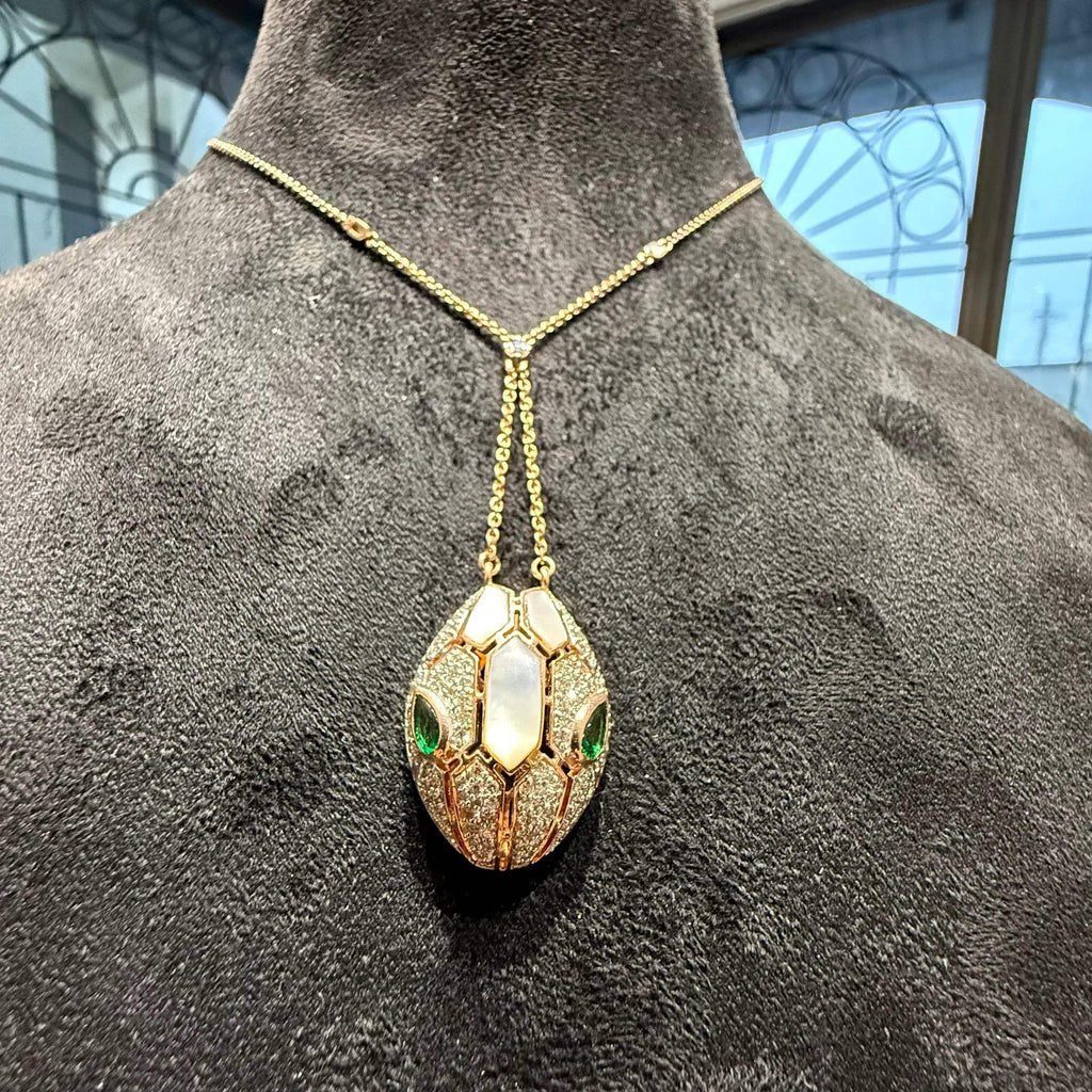 Oval-shaped gold diamond pendant with emerald green accents and mosaic design on a fine gold chain.