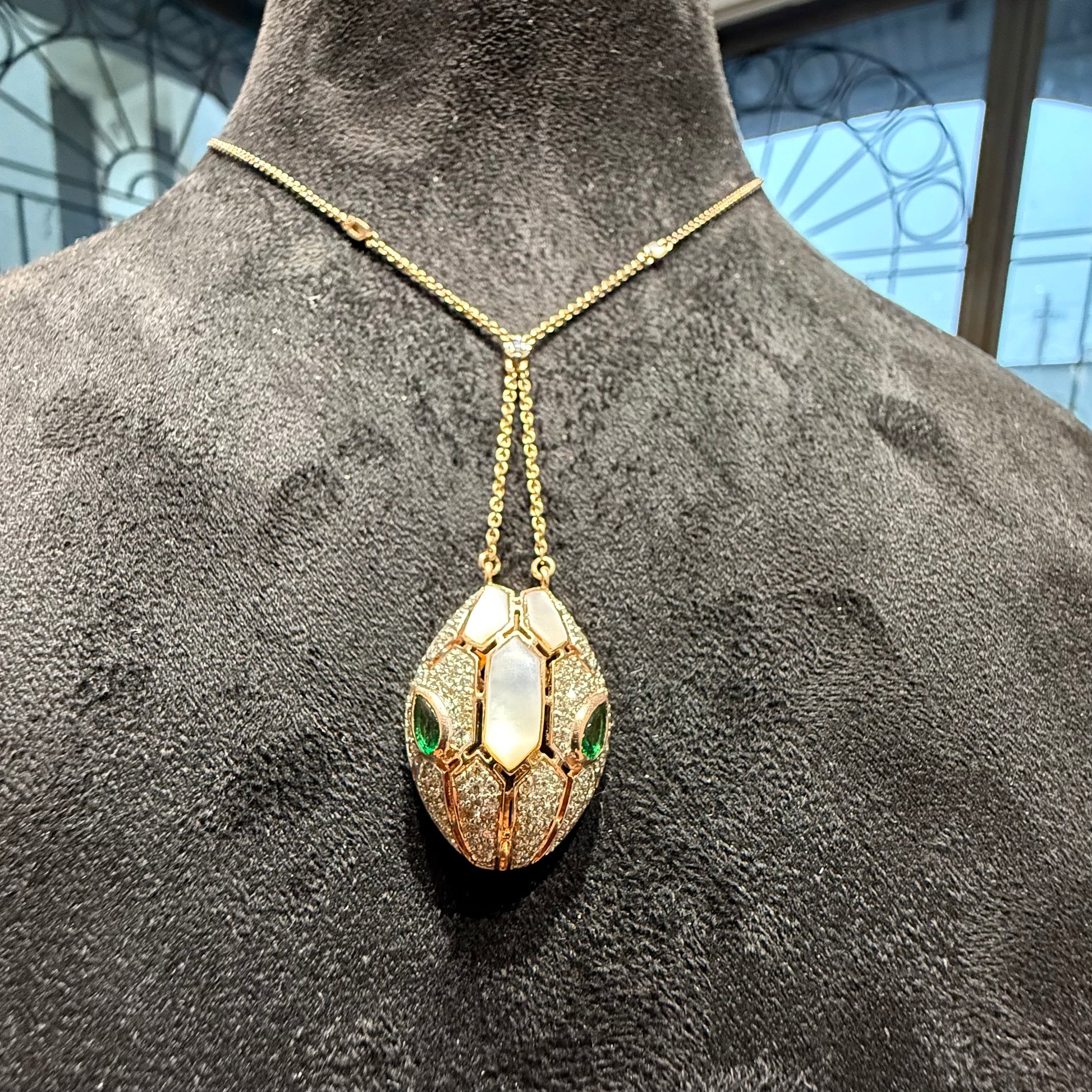 Oval-shaped gold diamond pendant with emerald green accents and mosaic design on a fine gold chain.