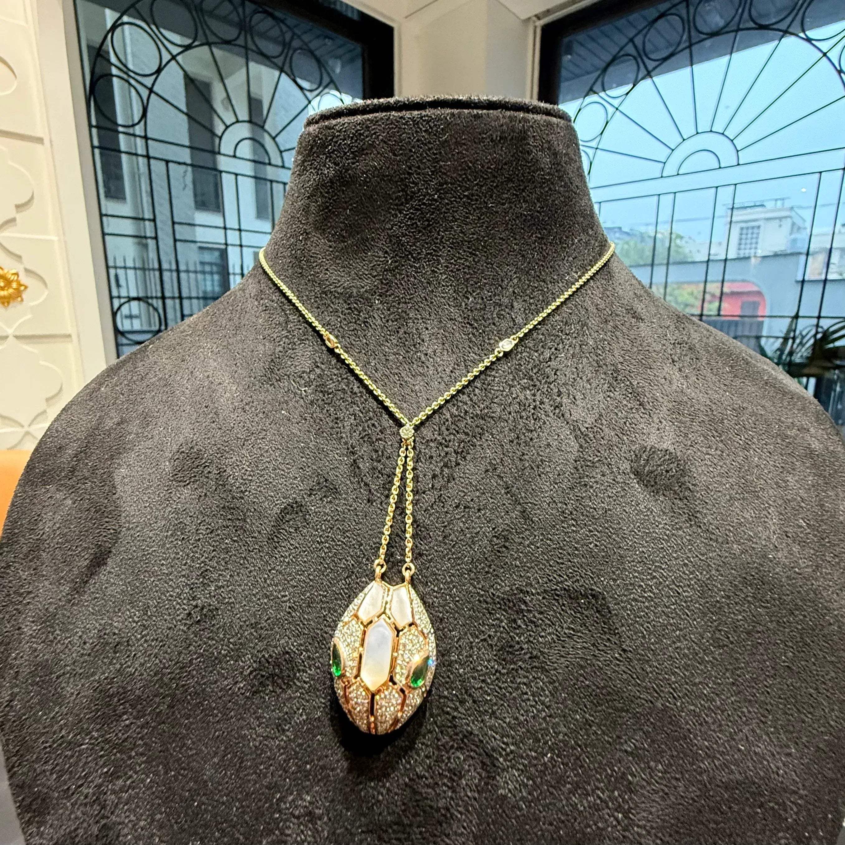 Oval-shaped gold diamond pendant with emerald green accents and mosaic design on a fine gold chain.
