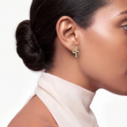 A close-up side profile of a woman with dark hair in a bun, wearing a small gold and diamond stud earring, against a clean white background.