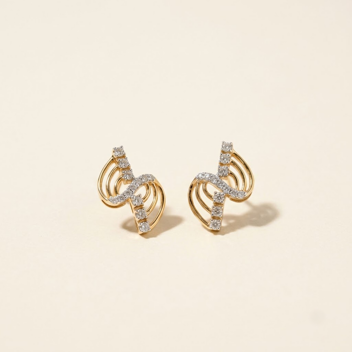 A pair of gold crescent-shaped stud earrings set with small clear stones, displayed on a warm cream background.