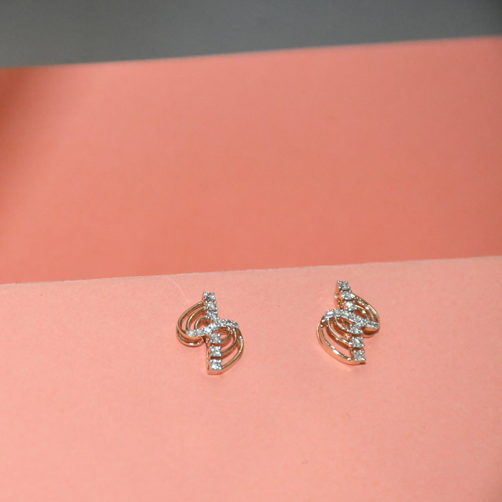 A pair of small gold-toned stud earrings with clear diamond accents, displayed on a peach-colored surface against a gray background.