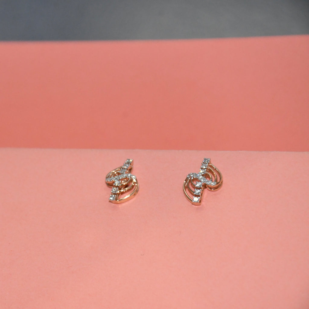A pair of small gold earrings with clear diamonds, displayed on a pink surface against a dark gray background.