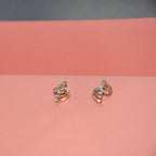 A pair of small gold earrings with clear diamonds, displayed on a pink surface against a dark gray background.