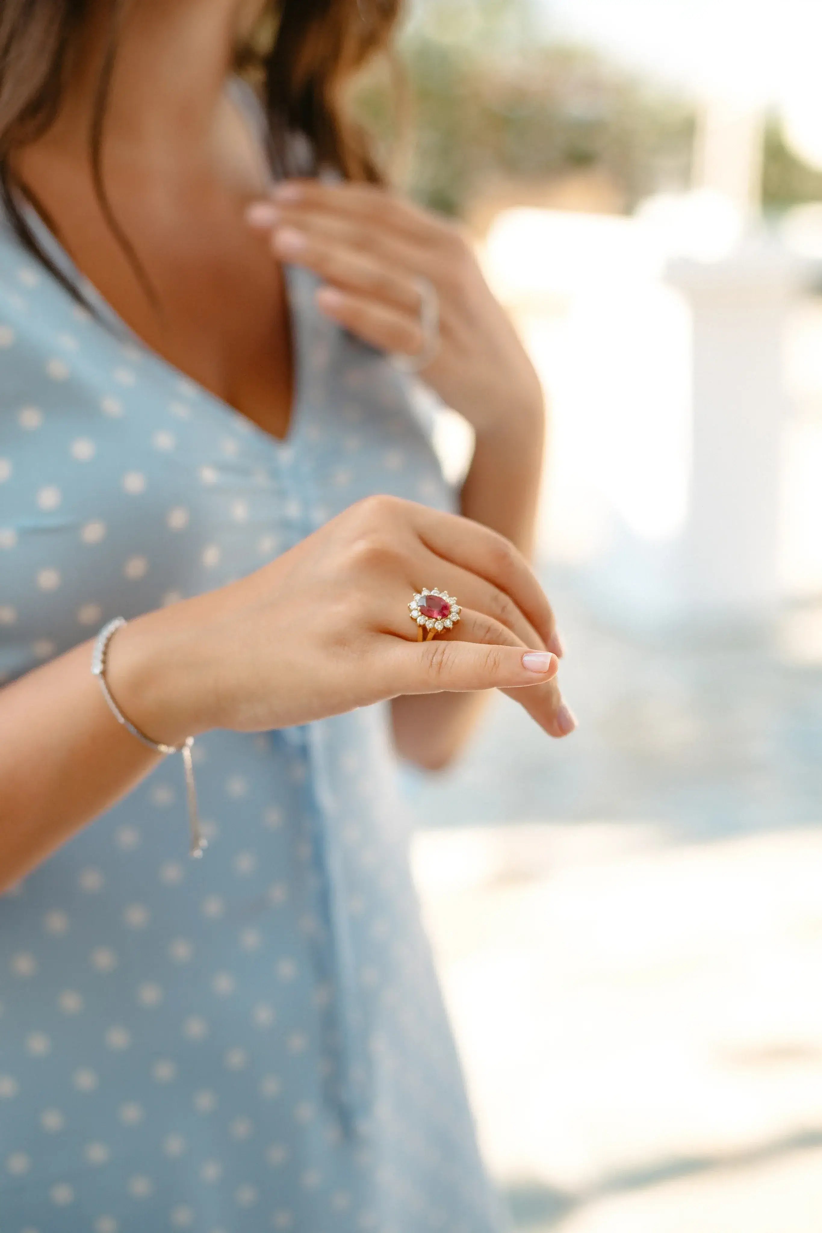 A women  is showing a red color stone and diamond ring worn in her finger. she also worn a diamond bracelet made with white gold.