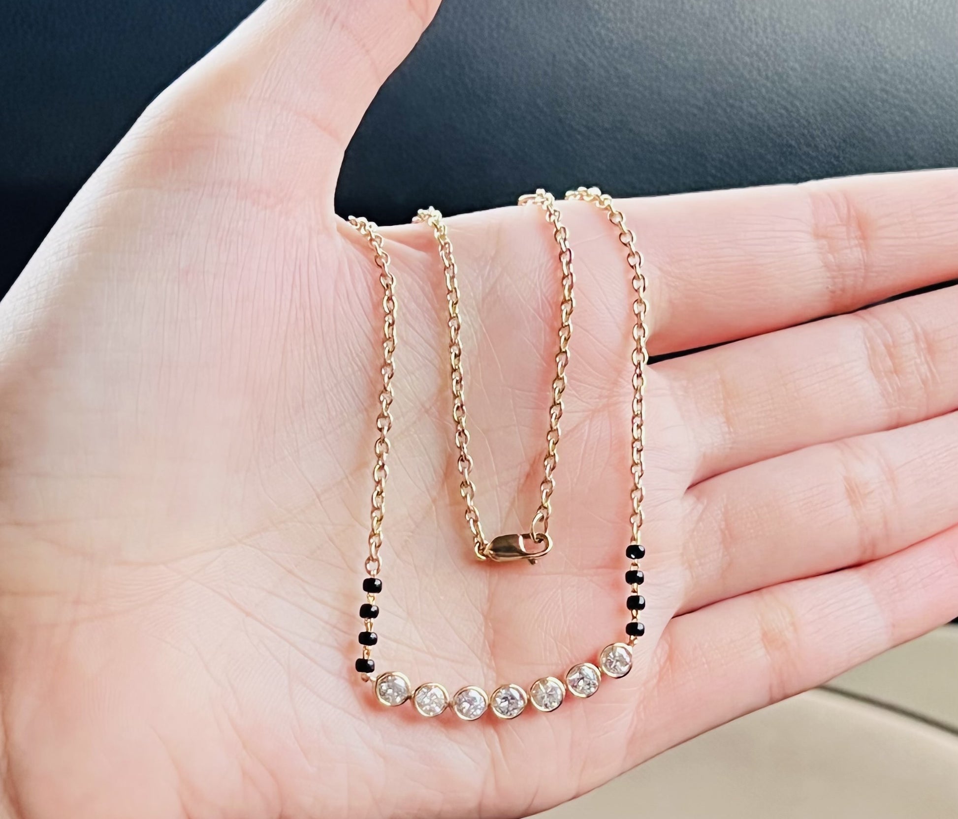 A stylish gold diamond beaded mangalsutra with seven round bezel-set diamonds in a row, paired with small black beads on a delicate gold chain.