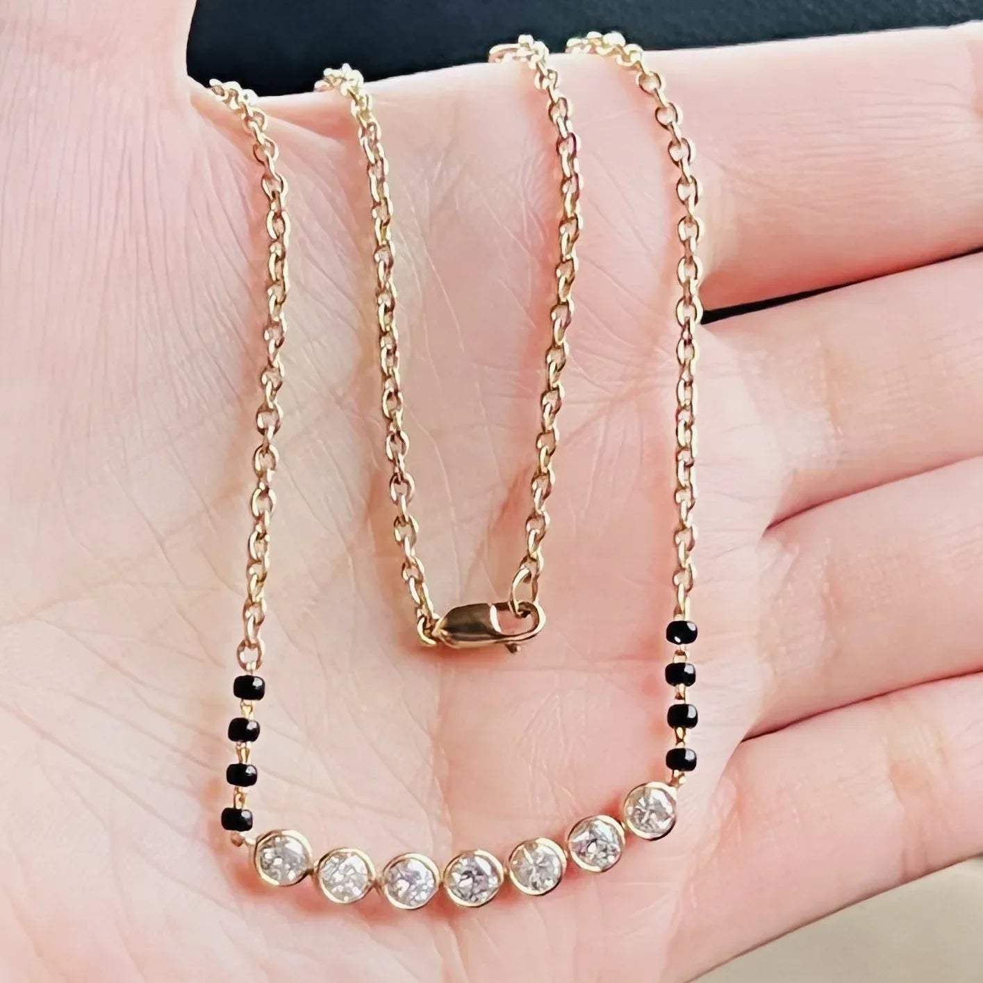 A stylish gold diamond beaded mangalsutra with seven round bezel-set diamonds in a row, paired with small black beads on a delicate gold chain.