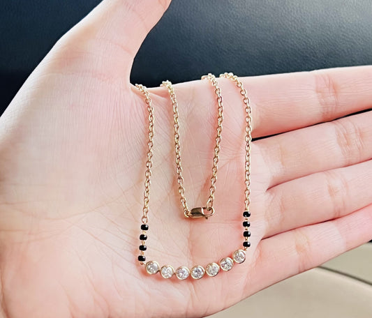 A stylish gold diamond beaded mangalsutra with seven round bezel-set diamonds in a row, paired with small black beads on a delicate gold chain.