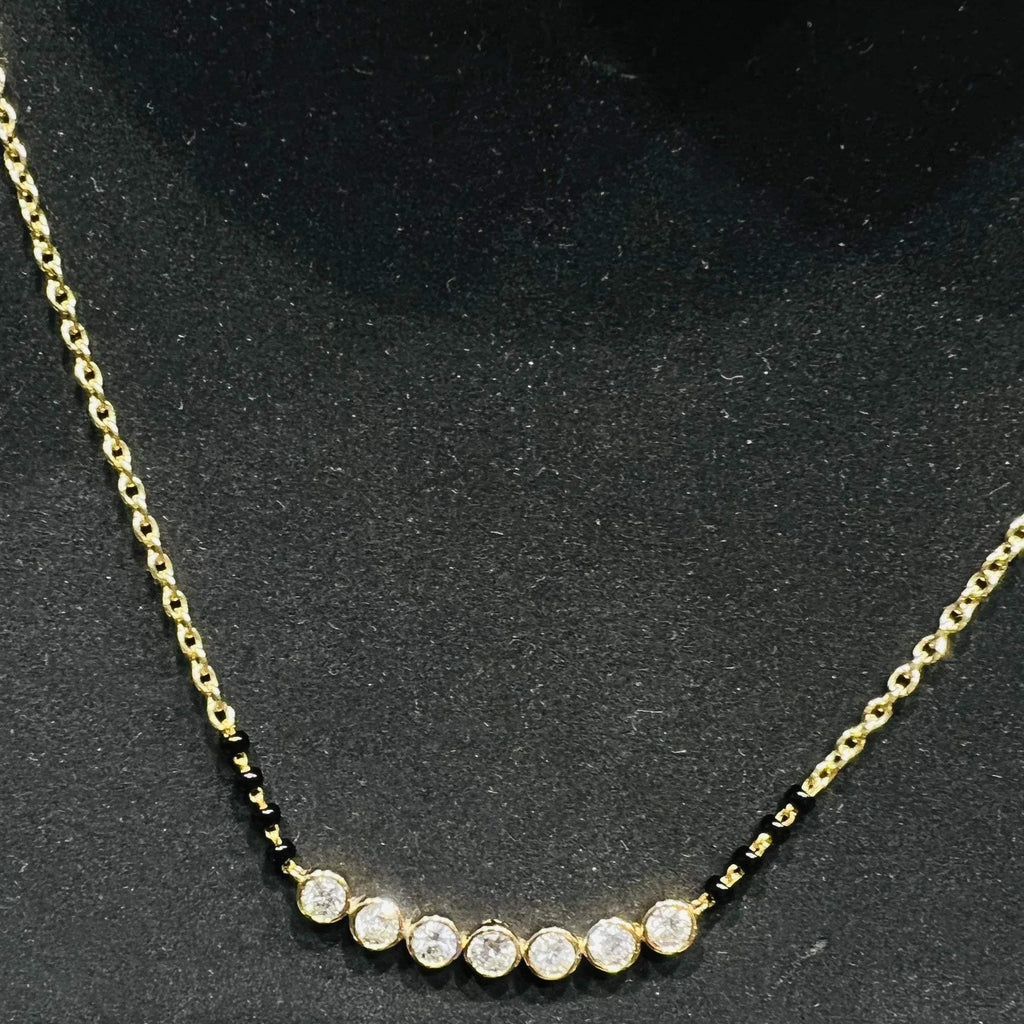 A stylish gold diamond beaded mangalsutra with seven round bezel-set diamonds in a row, paired with small black beads on a delicate gold chain.