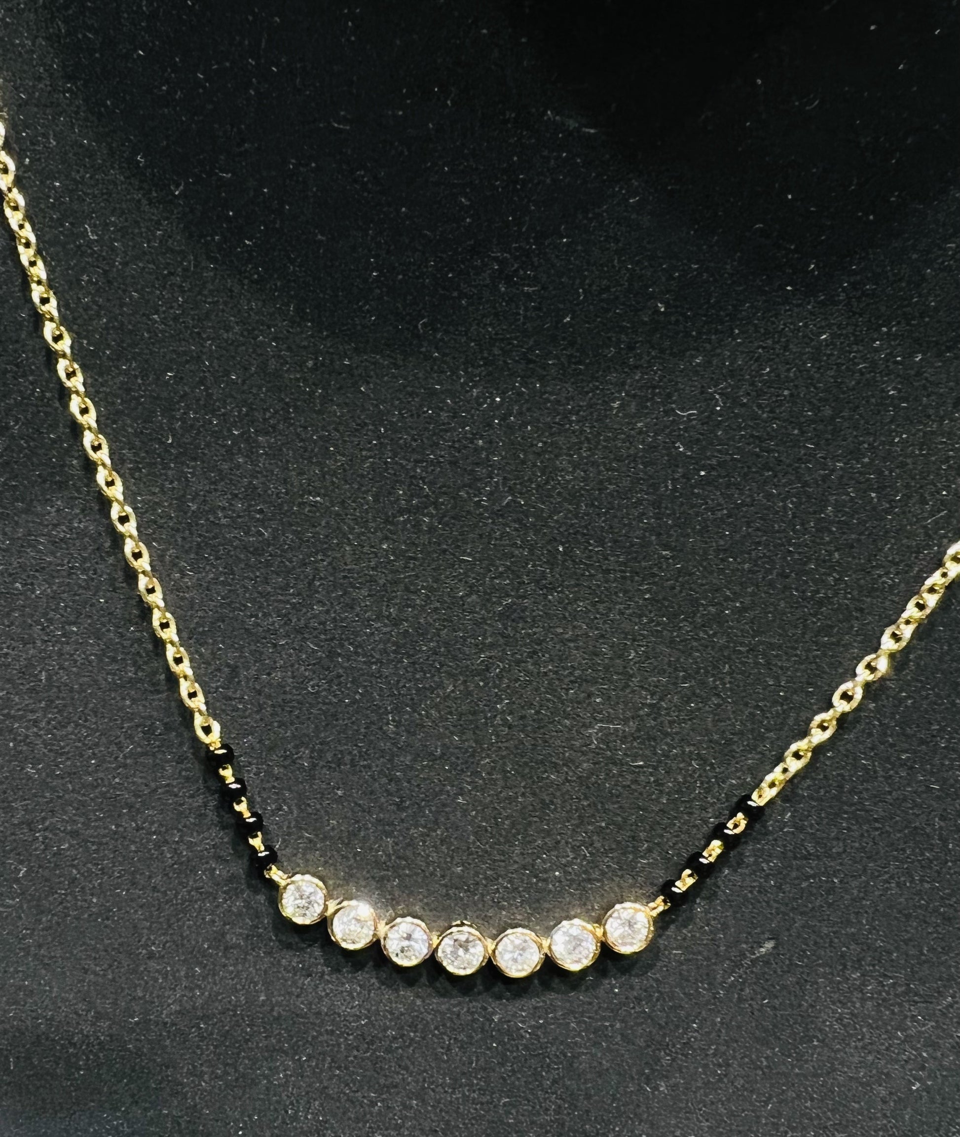 A stylish gold diamond beaded mangalsutra with seven round bezel-set diamonds in a row, paired with small black beads on a delicate gold chain.