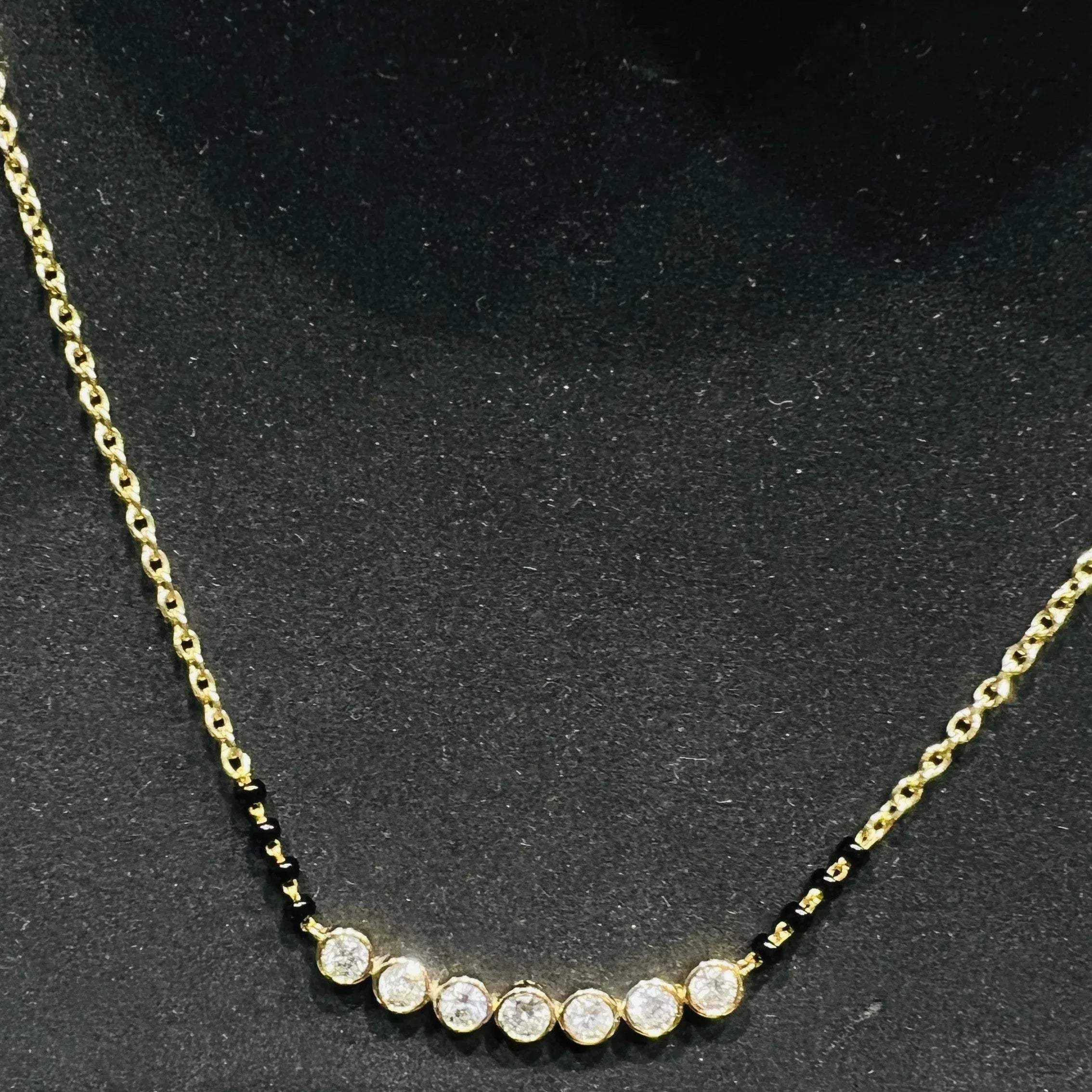 A stylish gold diamond beaded mangalsutra with seven round bezel-set diamonds in a row, paired with small black beads on a delicate gold chain.