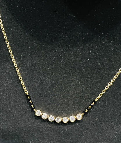 A stylish gold diamond beaded mangalsutra with seven round bezel-set diamonds in a row, paired with small black beads on a delicate gold chain.