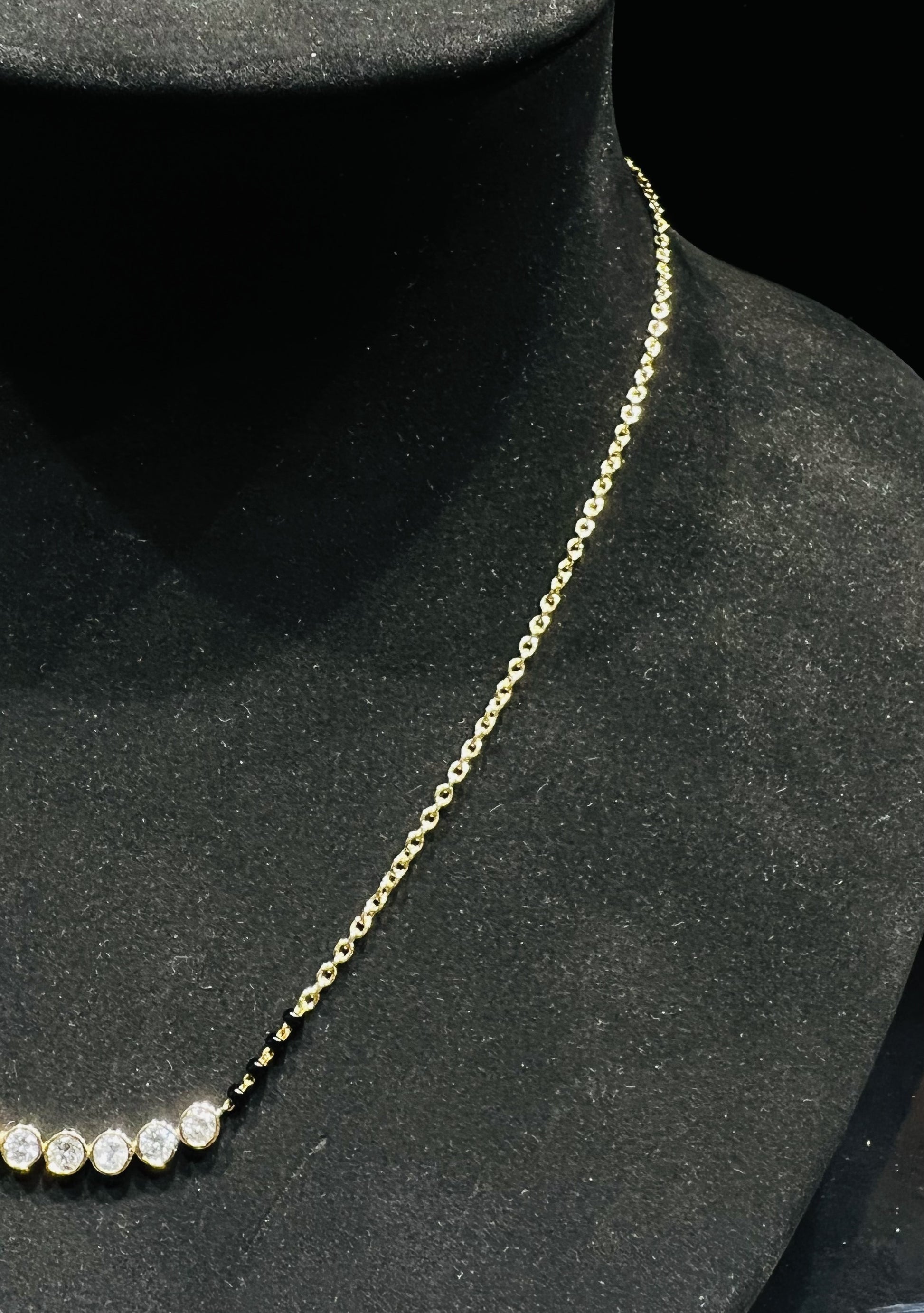 A stylish gold diamond beaded mangalsutra with seven round bezel-set diamonds in a row, paired with small black beads on a delicate gold chain.