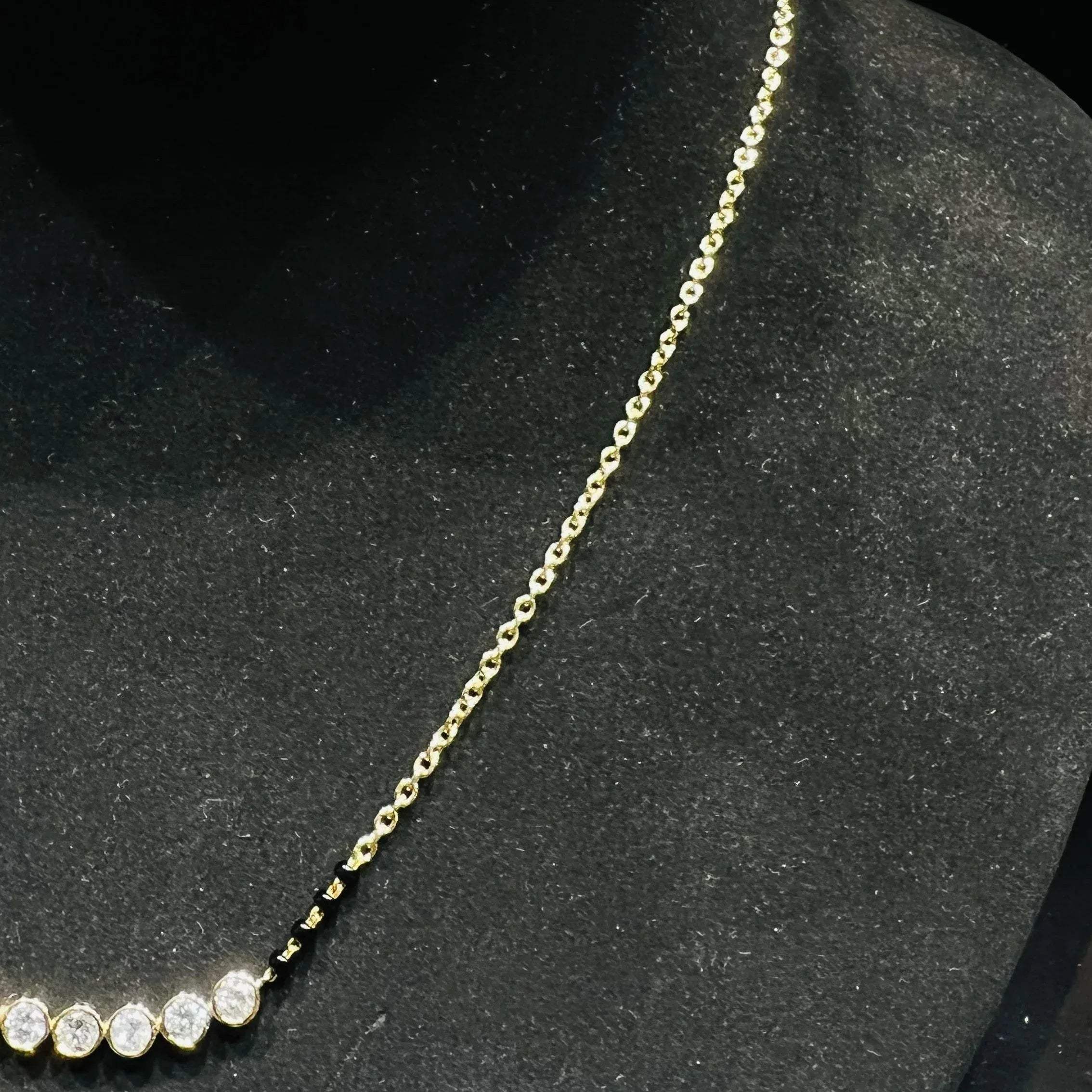 A stylish gold diamond beaded mangalsutra with seven round bezel-set diamonds in a row, paired with small black beads on a delicate gold chain.