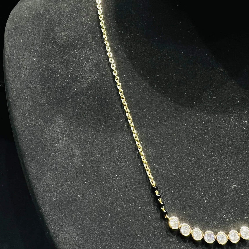 A stylish gold diamond beaded mangalsutra with seven round bezel-set diamonds in a row, paired with small black beads on a delicate gold chain.