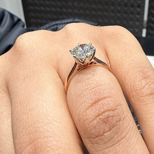 A classic solitaire lab grown diamond ring with a round-cut diamond set in a four-prong gold band shown in a hand.