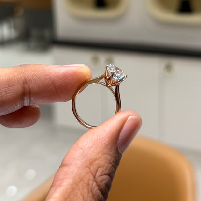 A classic solitaire lab grown diamond ring with a round-cut diamond set in a four-prong gold band, held between 2 fingers.