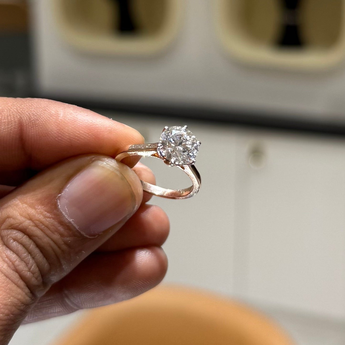 A classic solitaire lab grown diamond ring with a round-cut diamond set in a four-prong gold band, displayed holding by a hand.