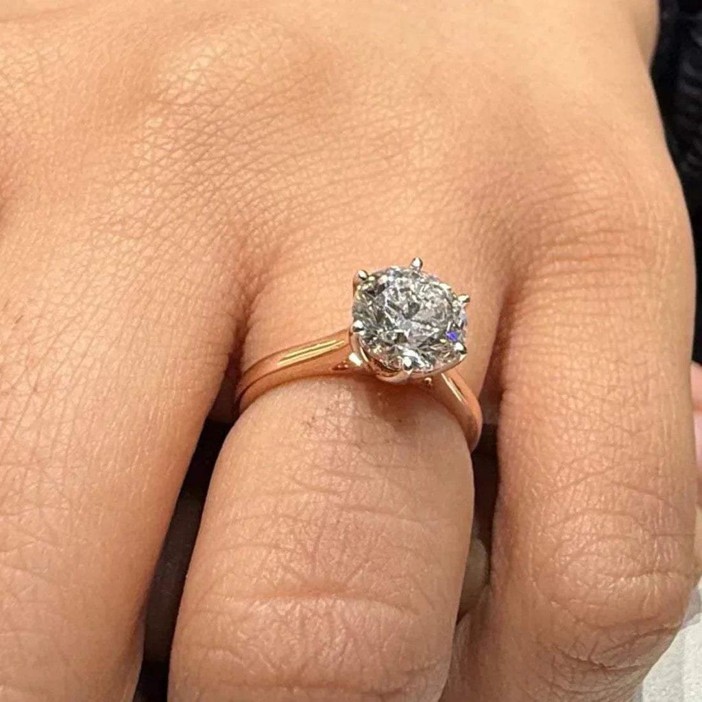 A classic solitaire lab grown diamond ring with a round-cut diamond set in a four-prong gold band, displayed worn in a hand's finger.