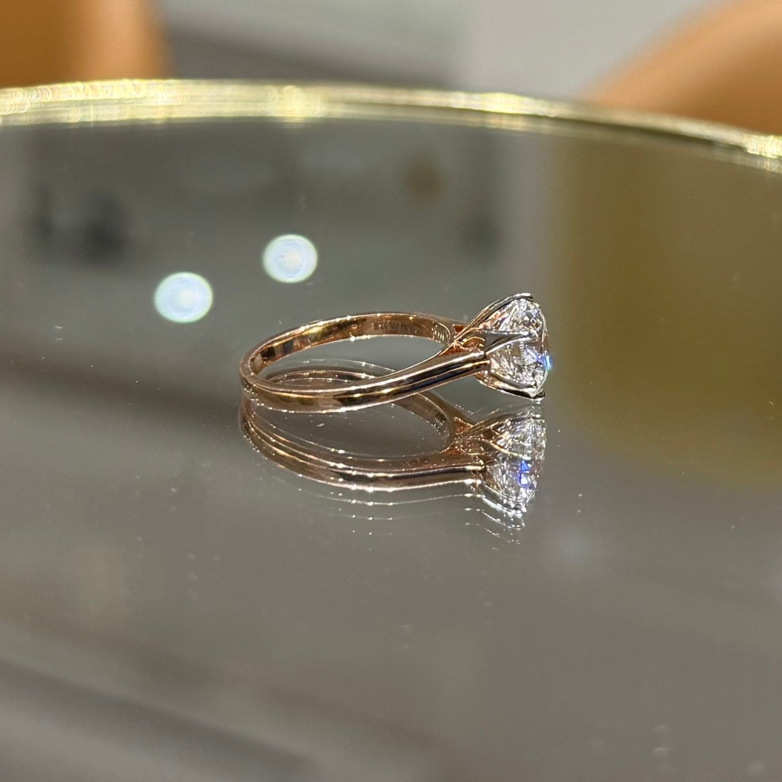A classic solitaire lab grown diamond ring with a round-cut diamond set in a four-prong gold band, displayed on a reflective surface.