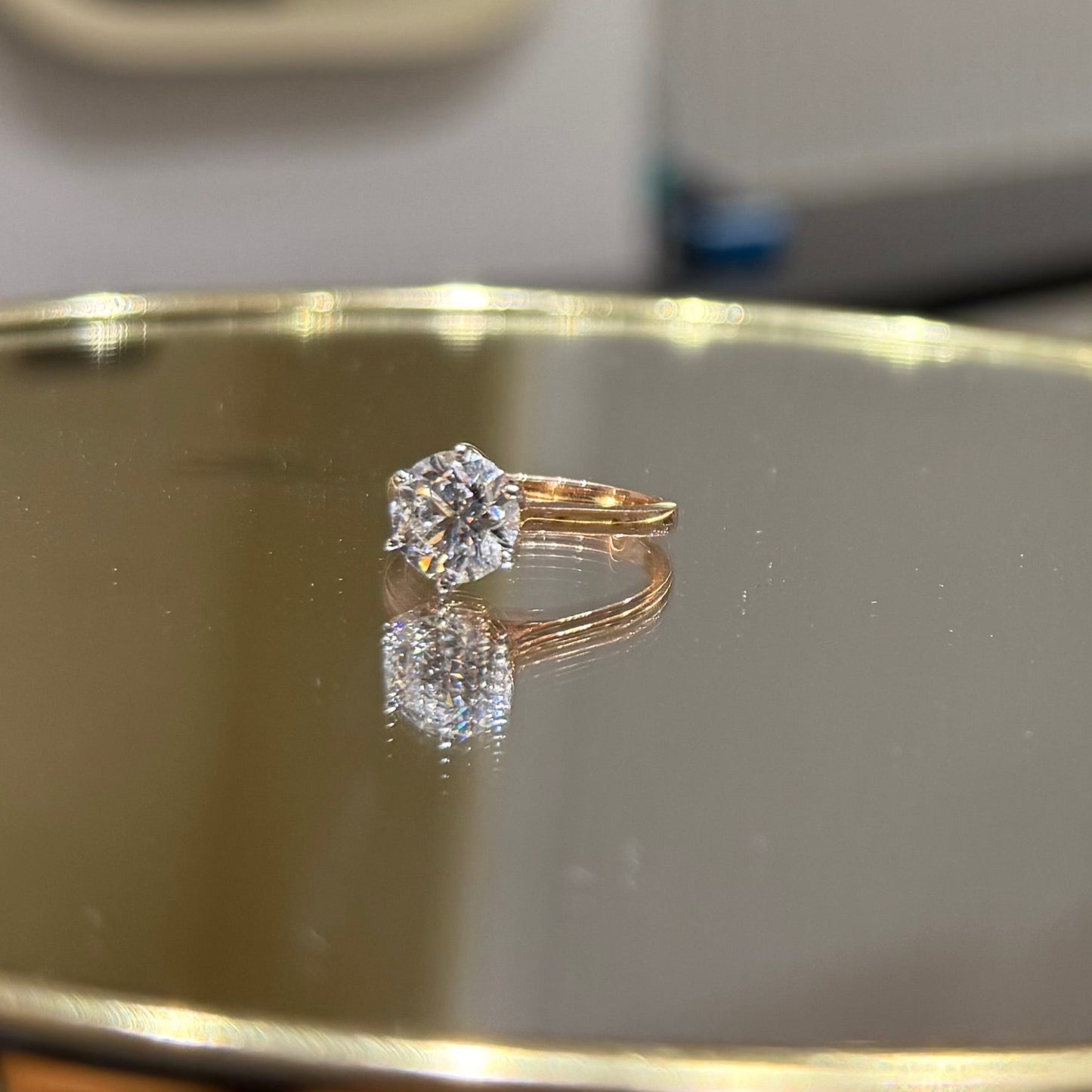 A classic solitaire lab grown diamond ring with a round-cut diamond set in a four-prong gold band, displayed on a reflective surface.