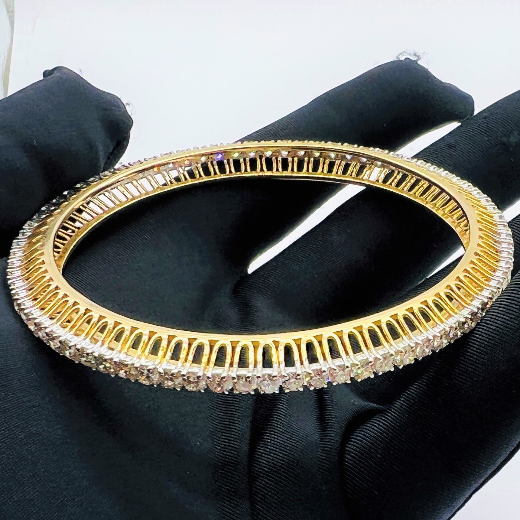 Gold bangles with lab grown diamond accents on a black gloves worn hand against a white background.
