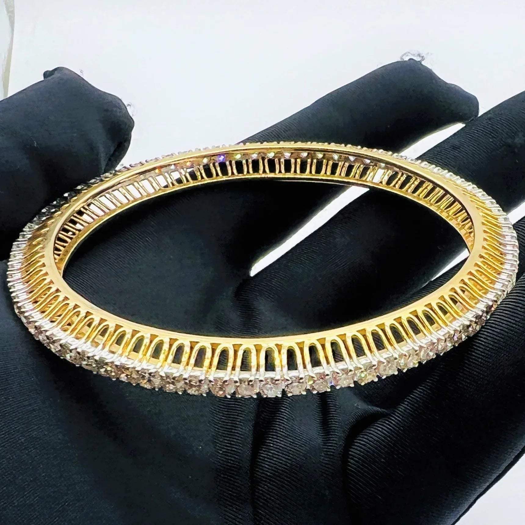 Gold bangles with lab grown diamond accents on a black gloves worn hand against a white background.