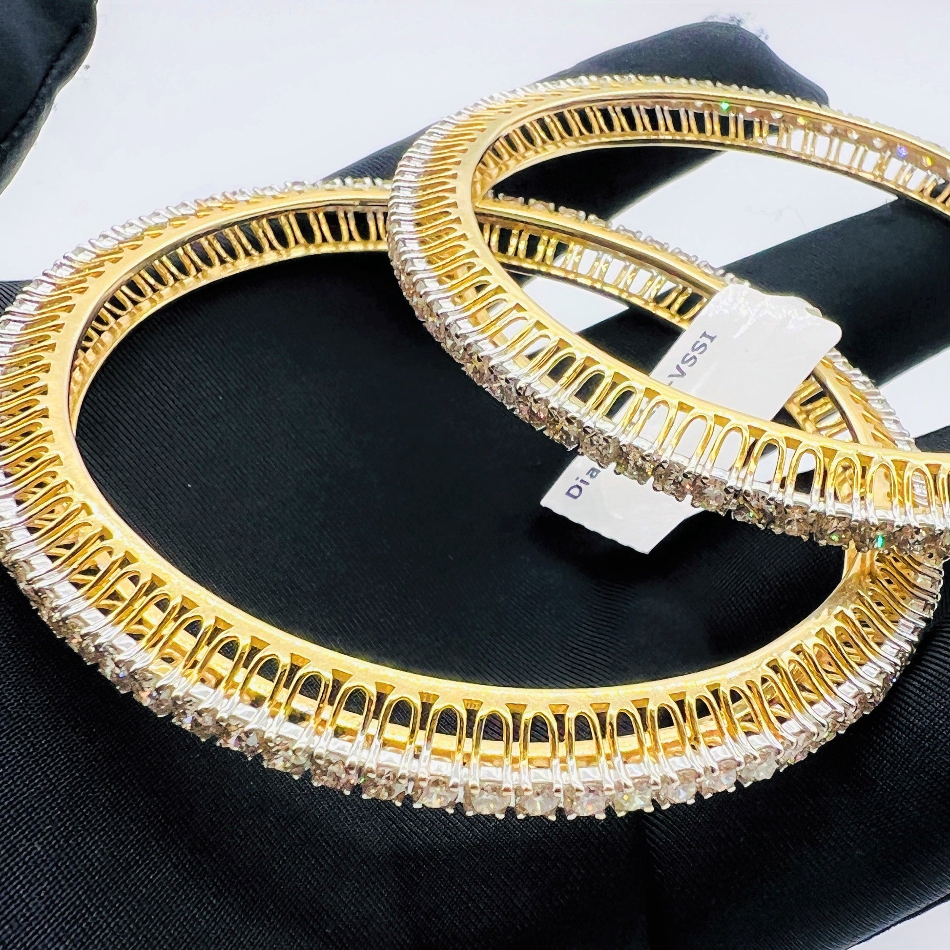 Two gold and lab grown diamond bangles on a black glove with a white background