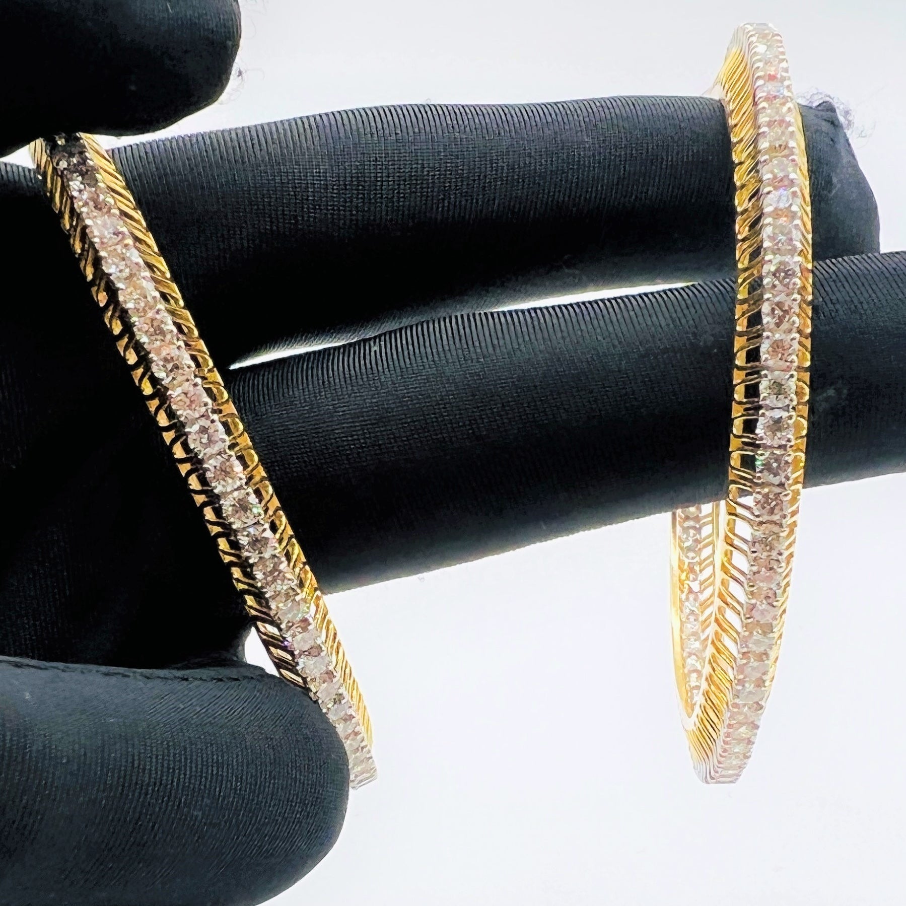 Gold bangles with lab grown diamond accents on a black gloves worn hand against a white background.