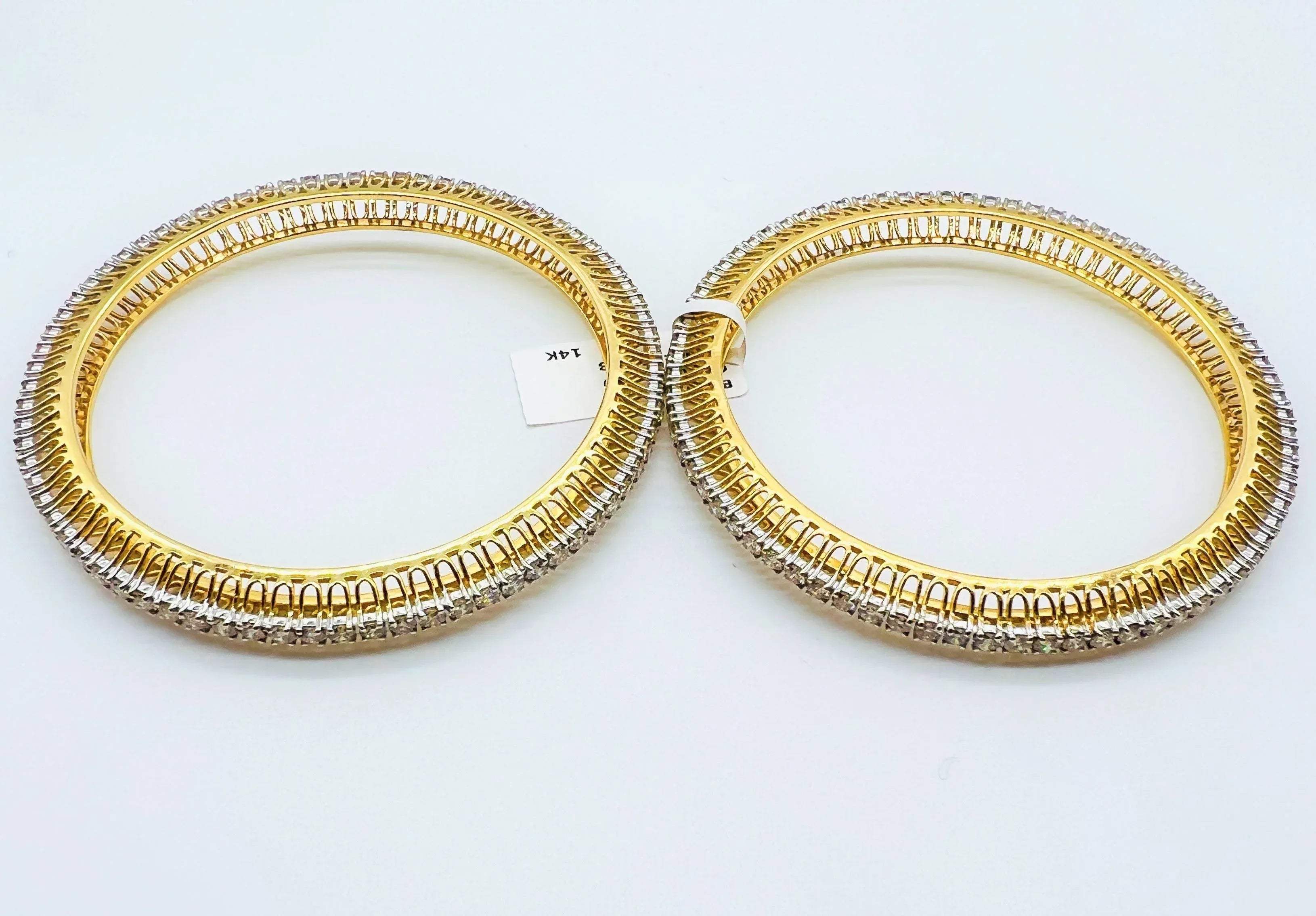 Two gold and lab grown diamond bangles on a white background