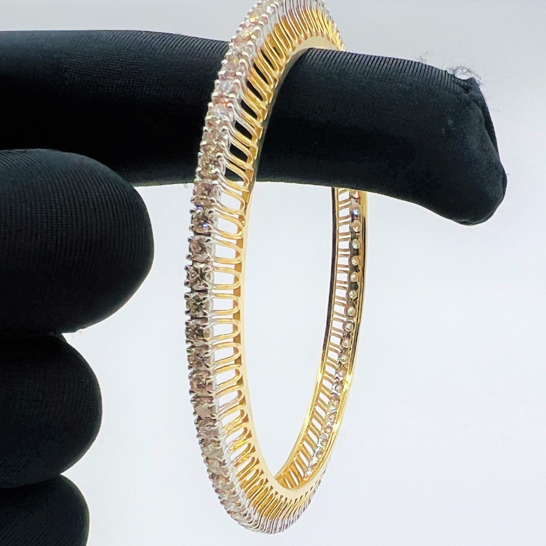 Gold bangles with lab grown diamond accents on a black stand against a white background