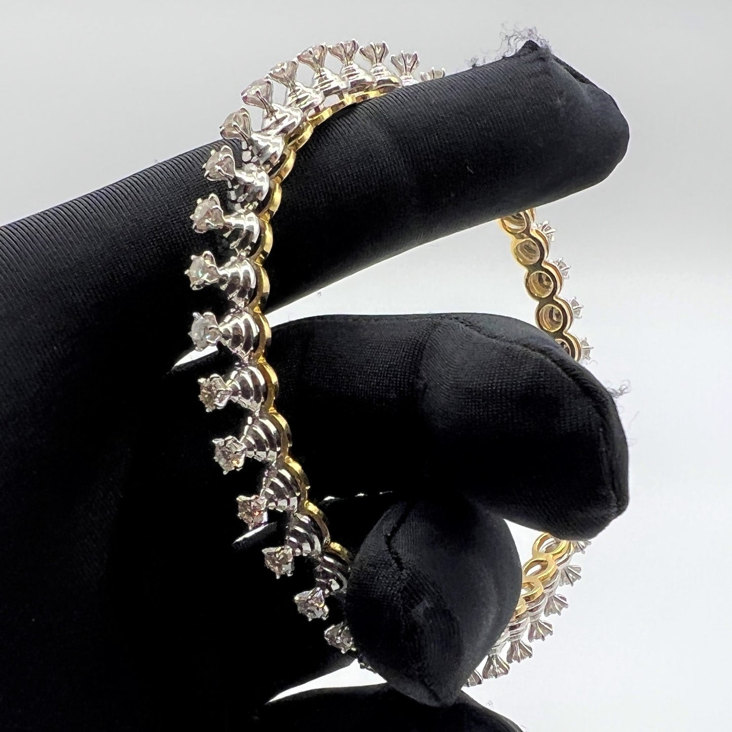 Gold and lab grown diamond bracelet held by a gloved hand against a gray background.
