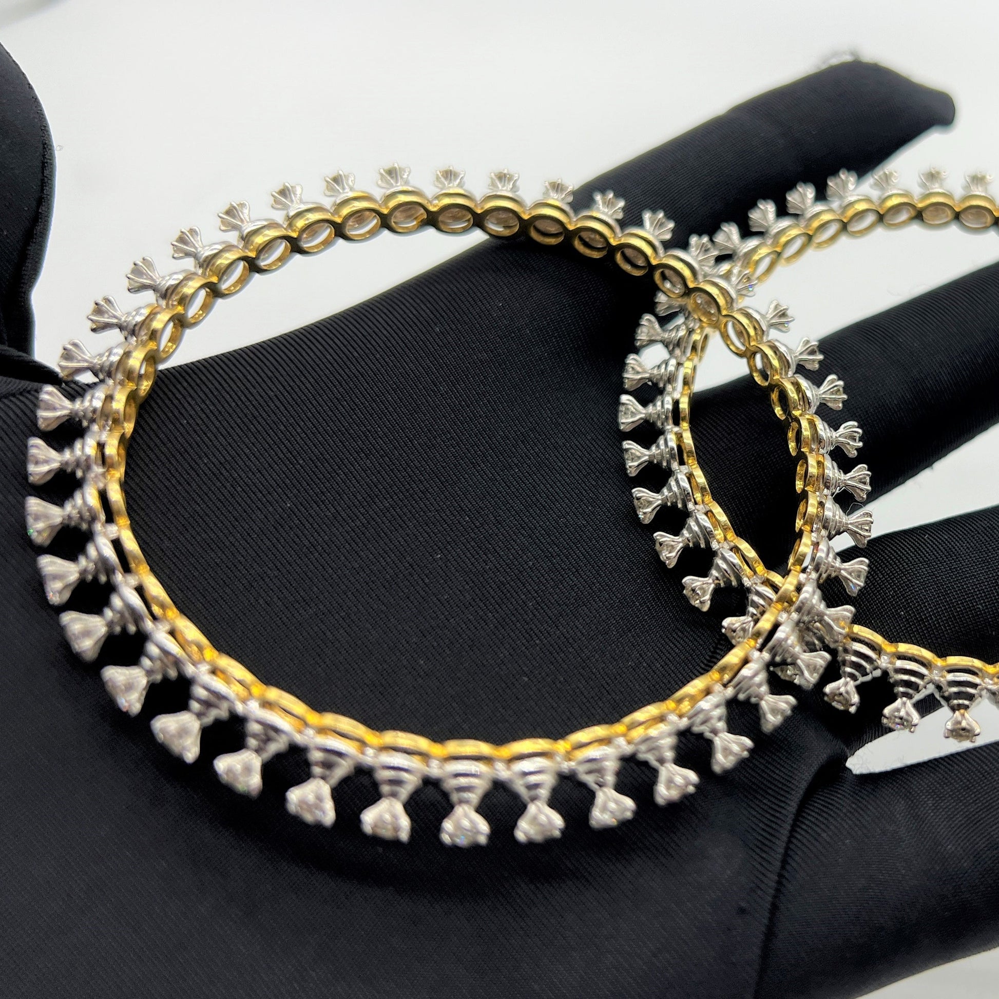 Gold and lab grown diamond bangles held by a gloved hand against a gray background.