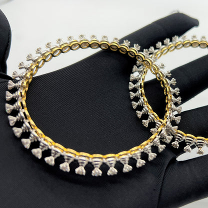 Gold and lab grown diamond bangles held by a gloved hand against a gray background.