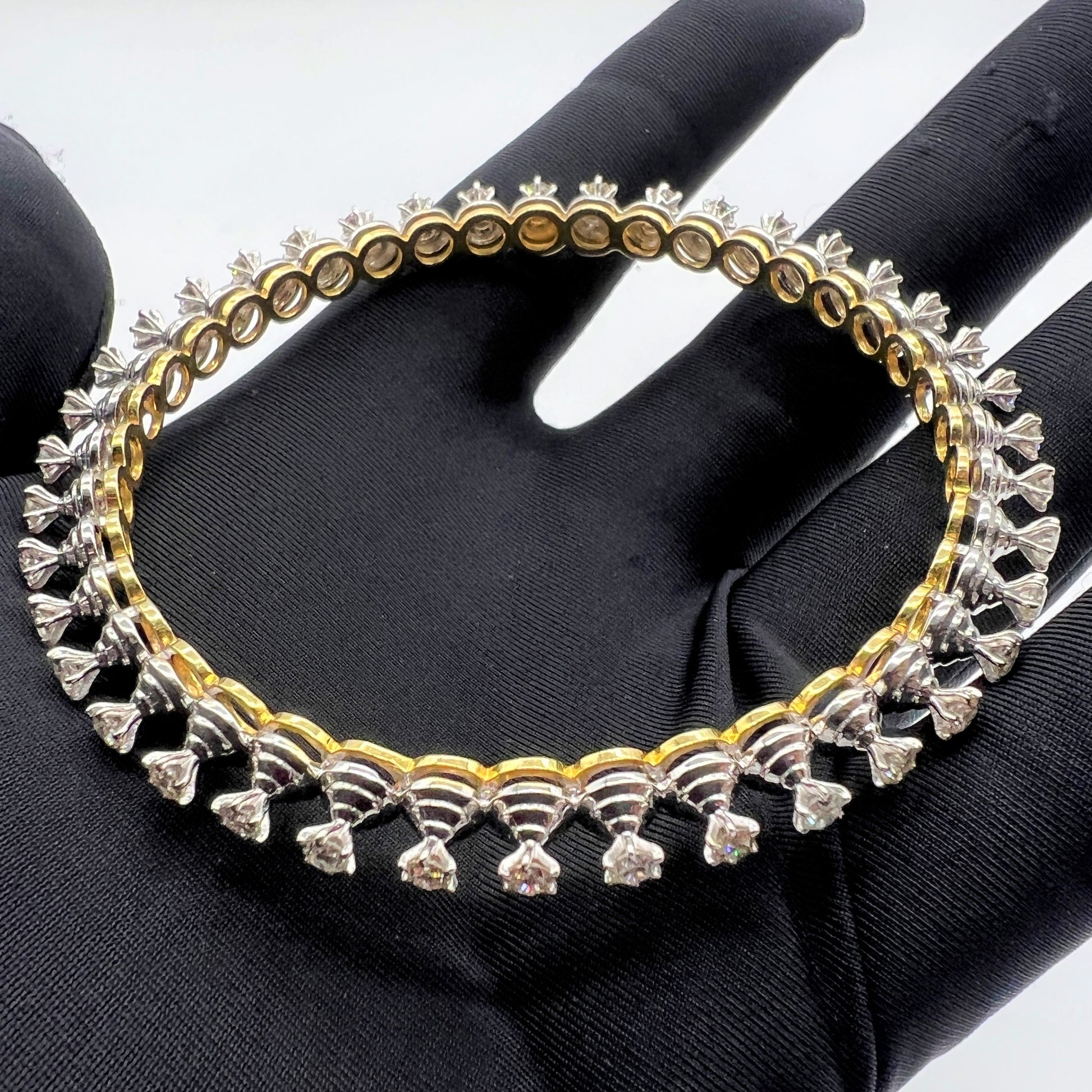 Gold and lab grown diamond bangle held by a gloved hand against a gray background